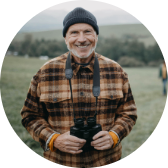 A man outside with binoculars smiling at the camera.